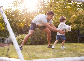 Far og søn spiller bold i haven. 
